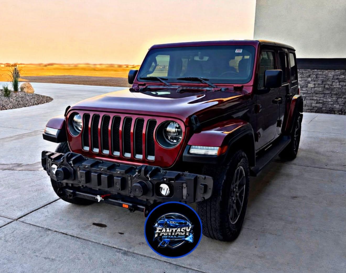 Glossy maroon four-door Jeep Wrangler parked on a concrete driveway during a golden sunset.