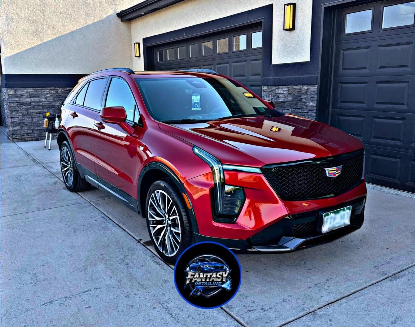 Shiny red Cadillac SUV parked on a driveway in front of a modern dark garage.
