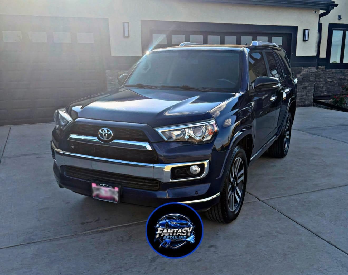 Gleaming dark blue Toyota 4Runner parked on a concrete driveway in front of a house.